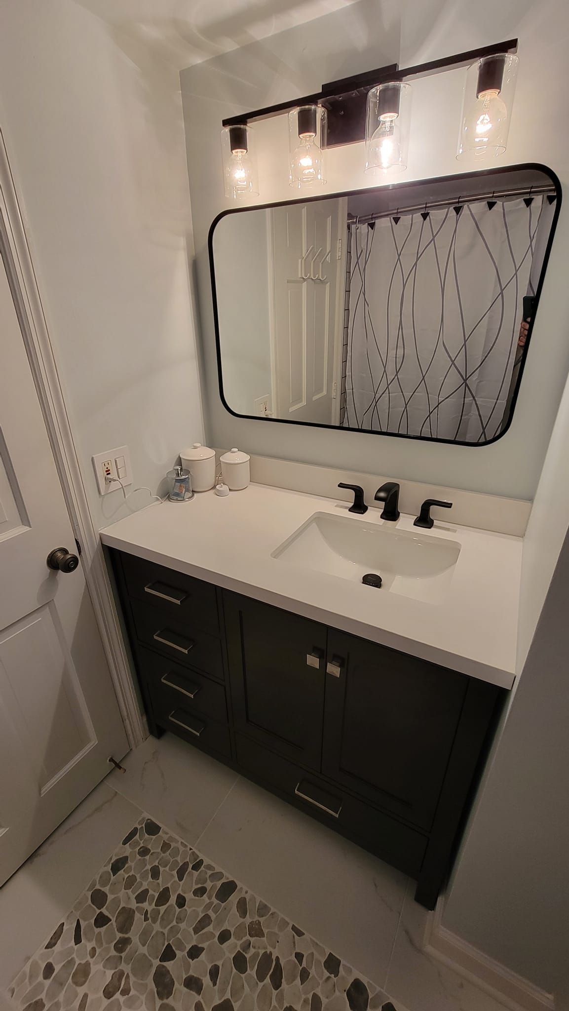A bathroom vanity with a dark wood cabinet, white countertop, black faucet, rectangular mirror, and overhead light.