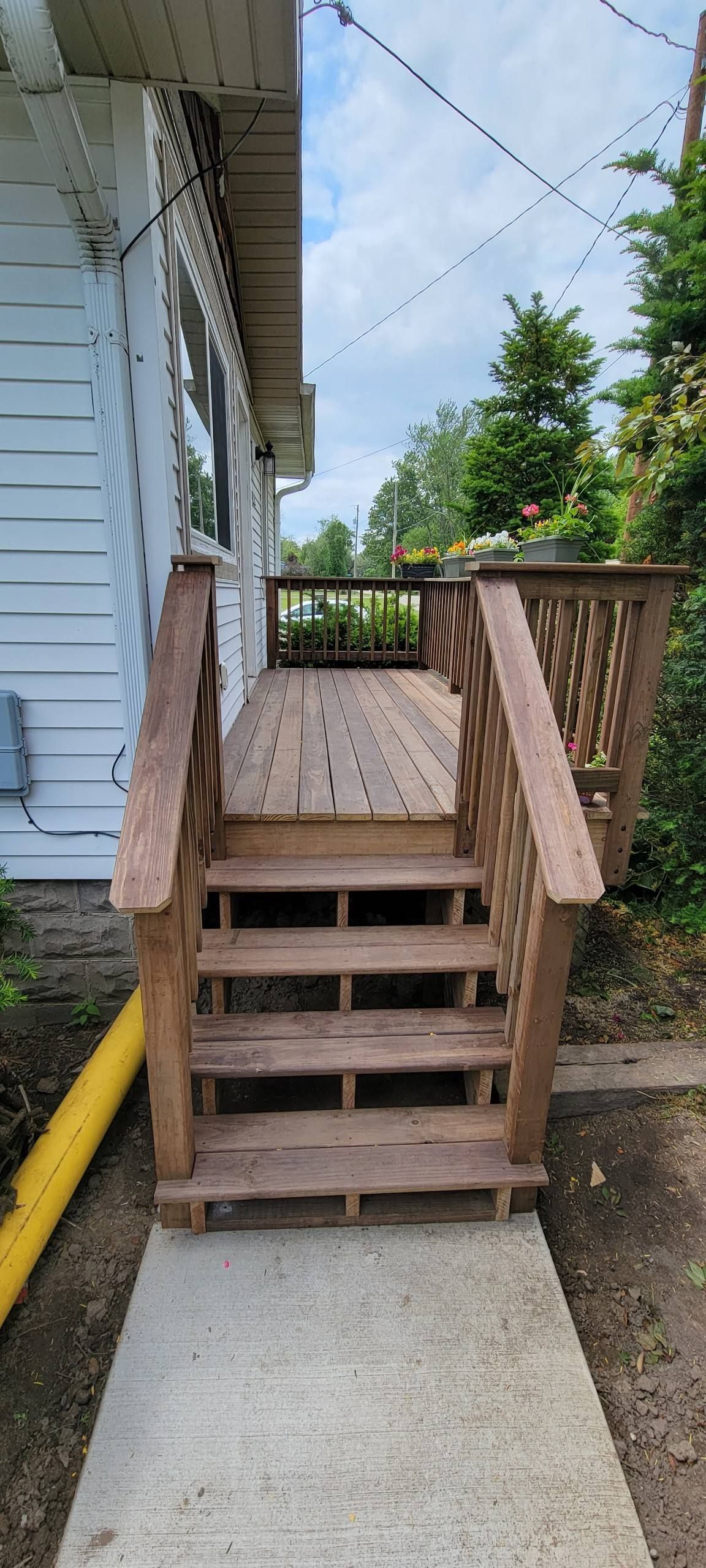 A short set of brown wooden stairs leading up to a wooden porch attached to the side of a white house.