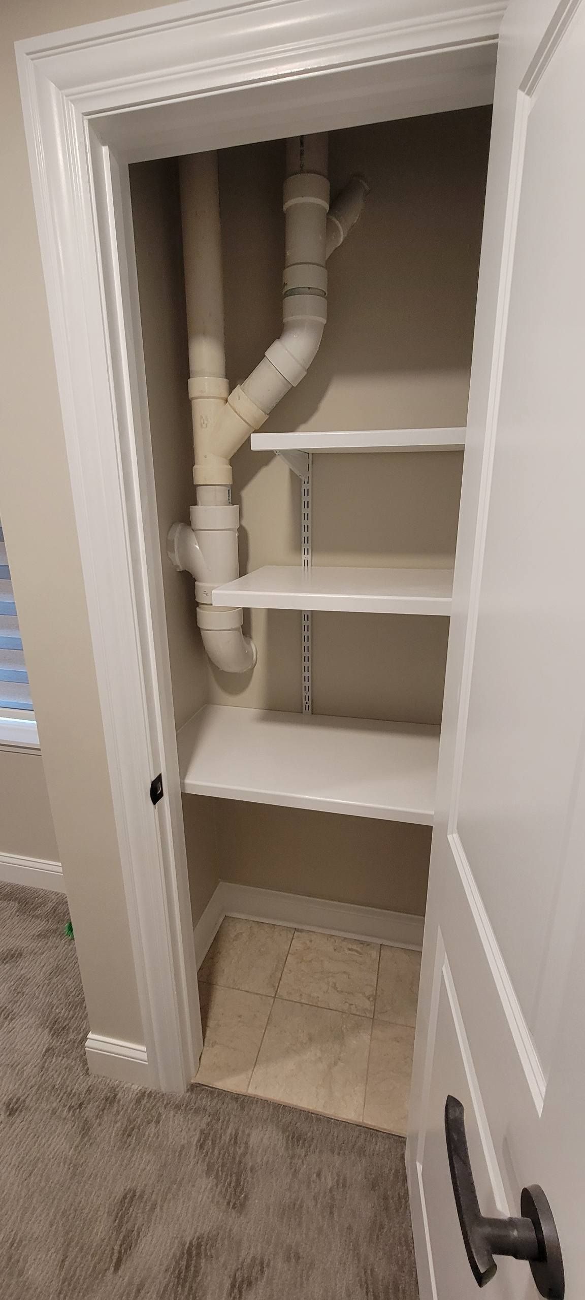 An open closet featuring white shelves with a white PVC plumbing pipe running vertically along the back wall.