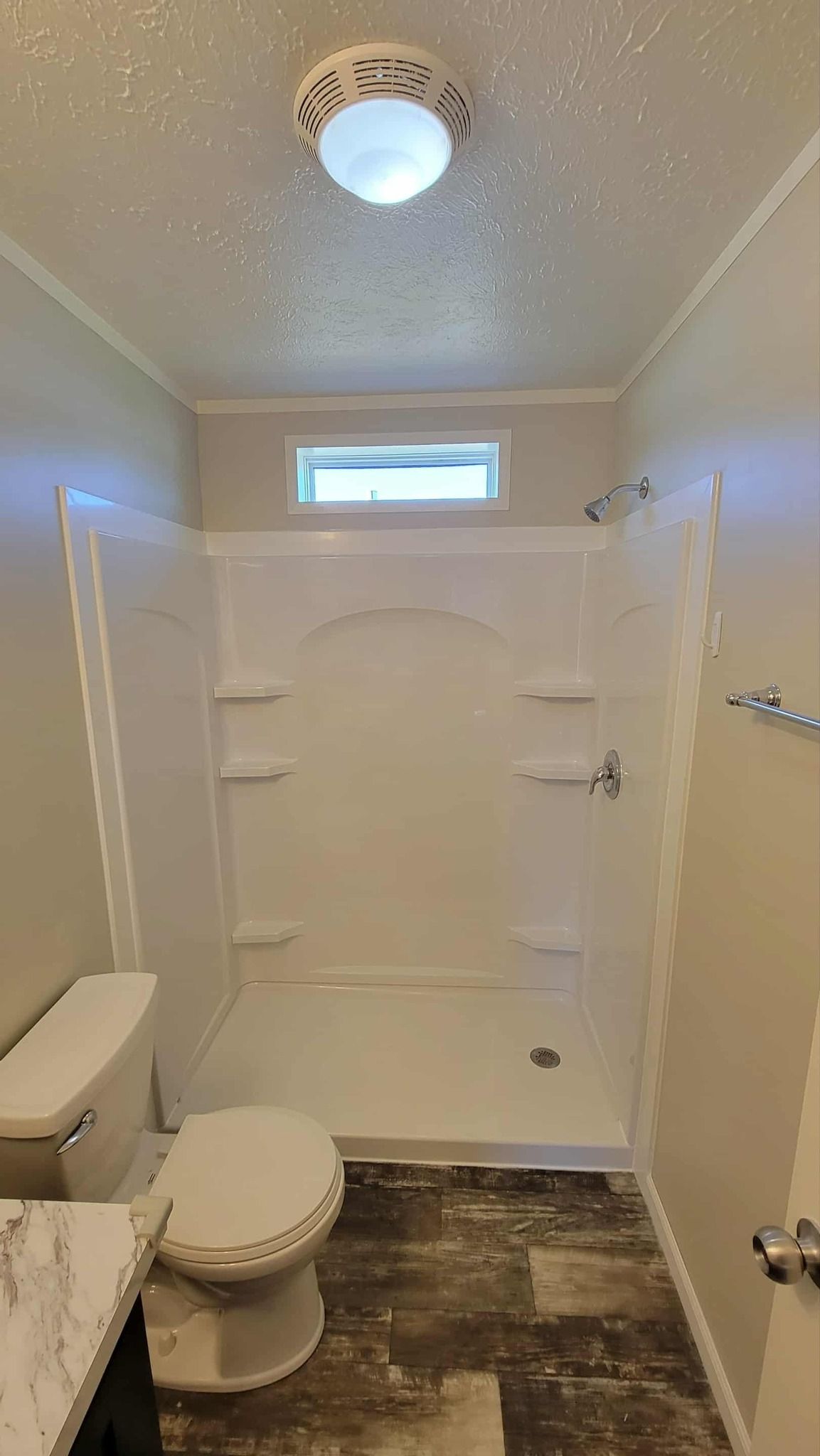 A small bathroom with a white shower stall, a toilet, a vanity counter, and a light fixture on the textured ceiling.
