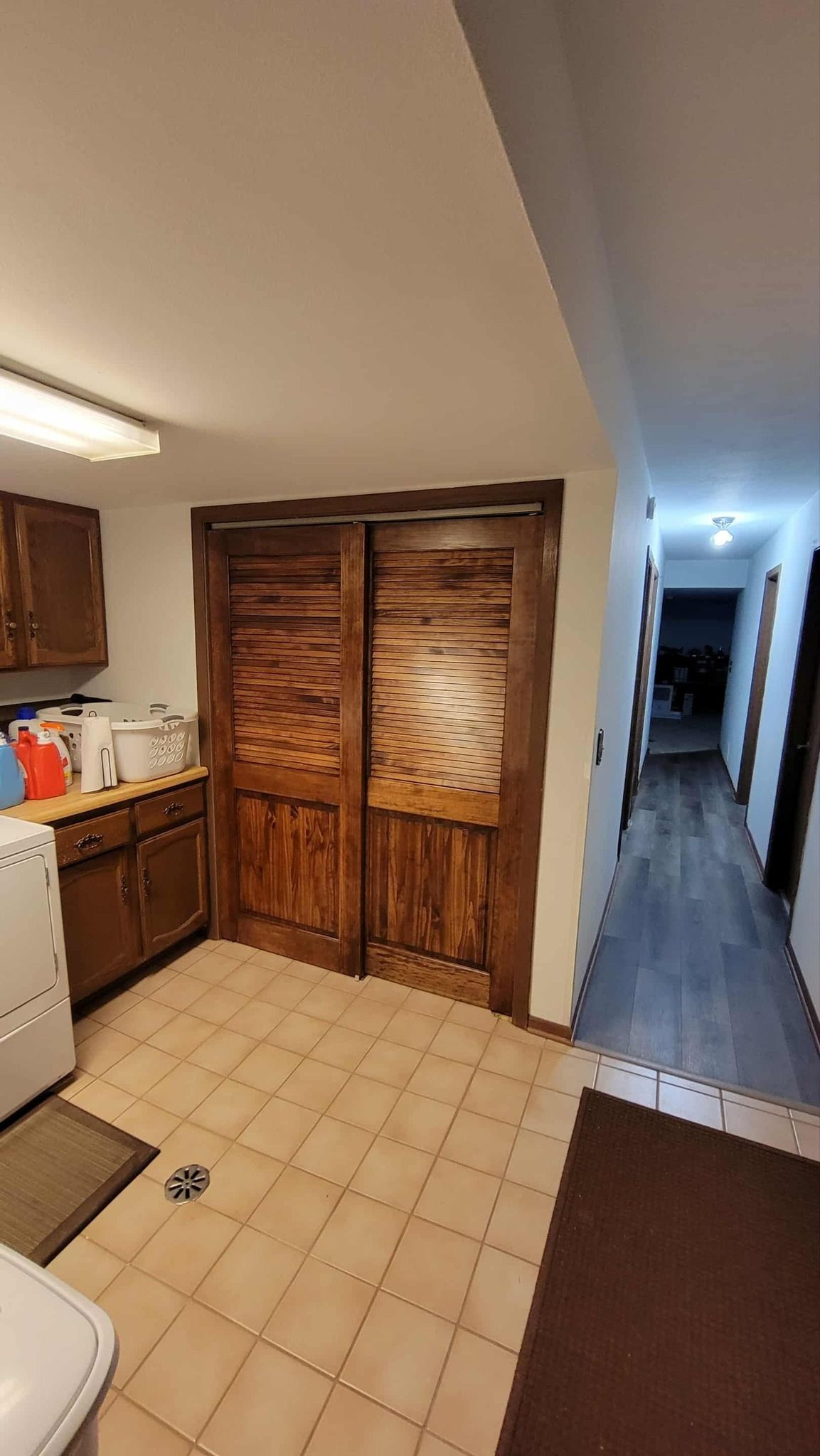 Kitchen area with wooden cabinets, beige tiled floor, sliding wooden doors, and a hallway leading to another room.