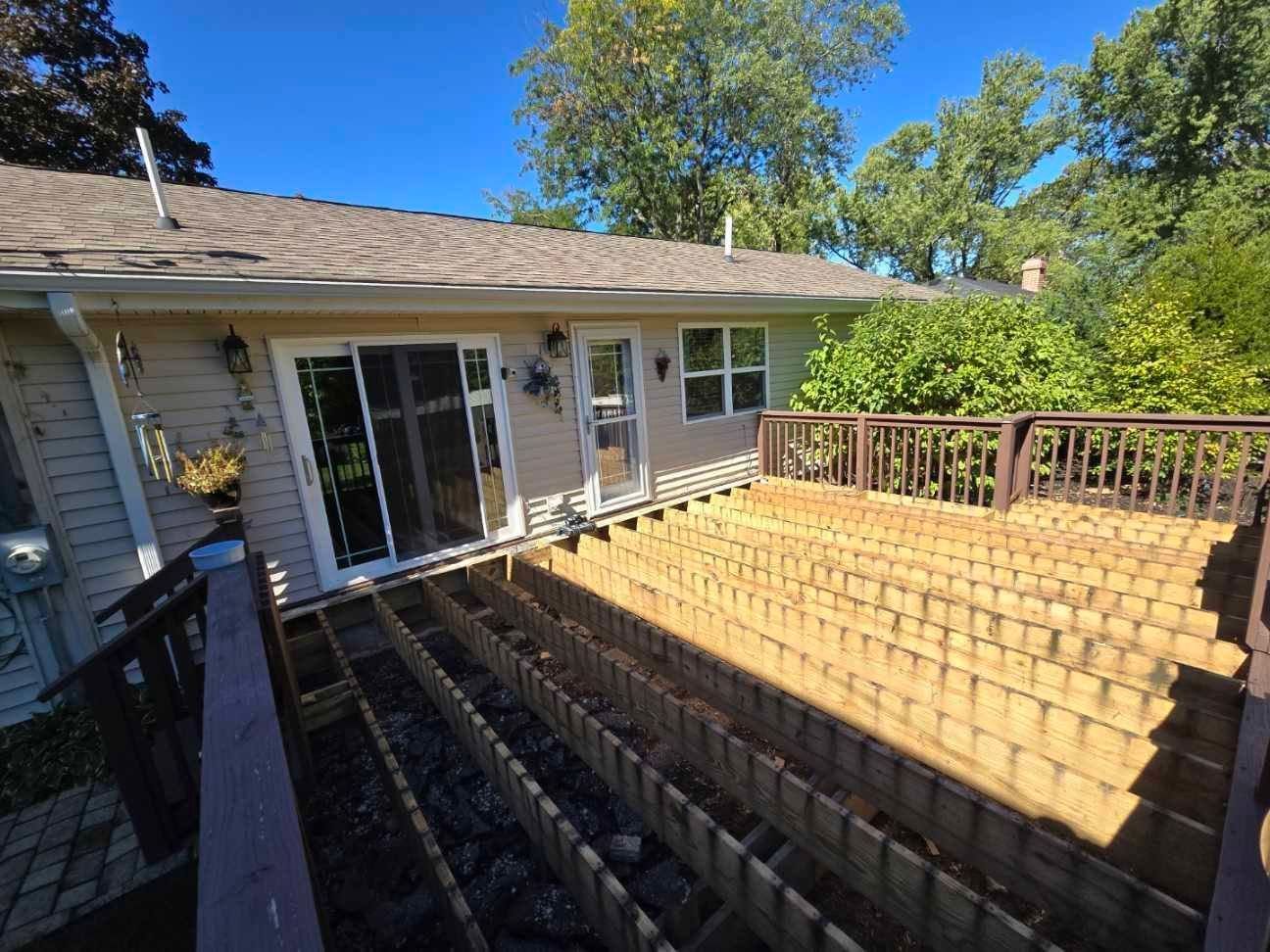 An elevated wooden deck frame with exposed floor joists attached to the back of a beige residential house.