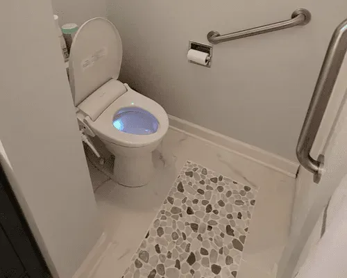 Accessible bathroom with a white toilet featuring an illuminated blue bowl, a bidet attachment, and a safety grab bar.