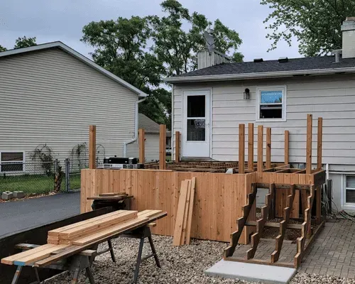 A wooden deck under construction attached to the back of a house, featuring exposed framing and a staircase in progress.