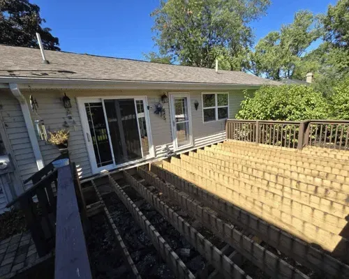A house with light siding and an unfinished wooden deck frame under a clear blue sky.