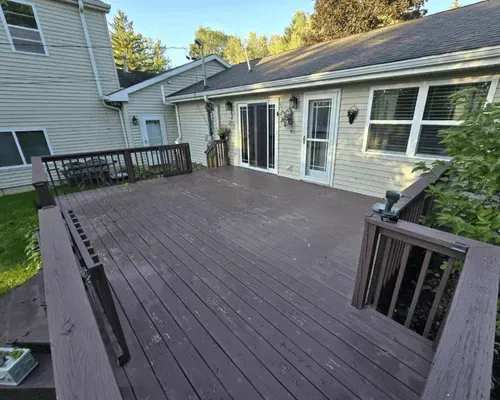 A large brown wooden deck with railing attached to the back of a light-colored two-story house.