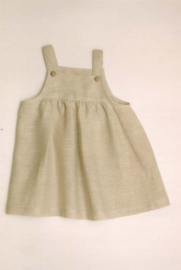 Bēša lina kleita ar pogām uz lencītēm atrodas uz baltas virsmas.