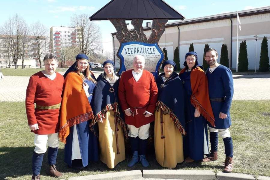 Cilvēku grupa pozē fotografēšanai pie zīmes ar uzrakstu