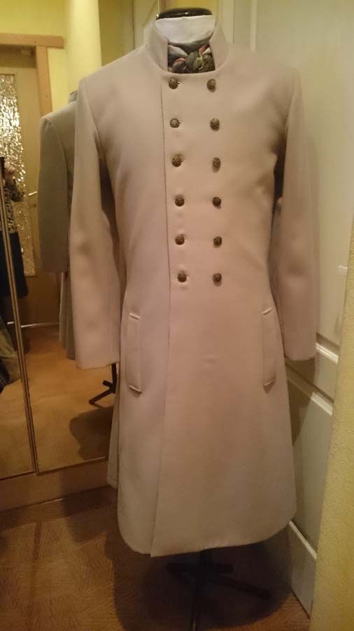 Uz manekena ir balts mētelis ar pogām un tauriņu.