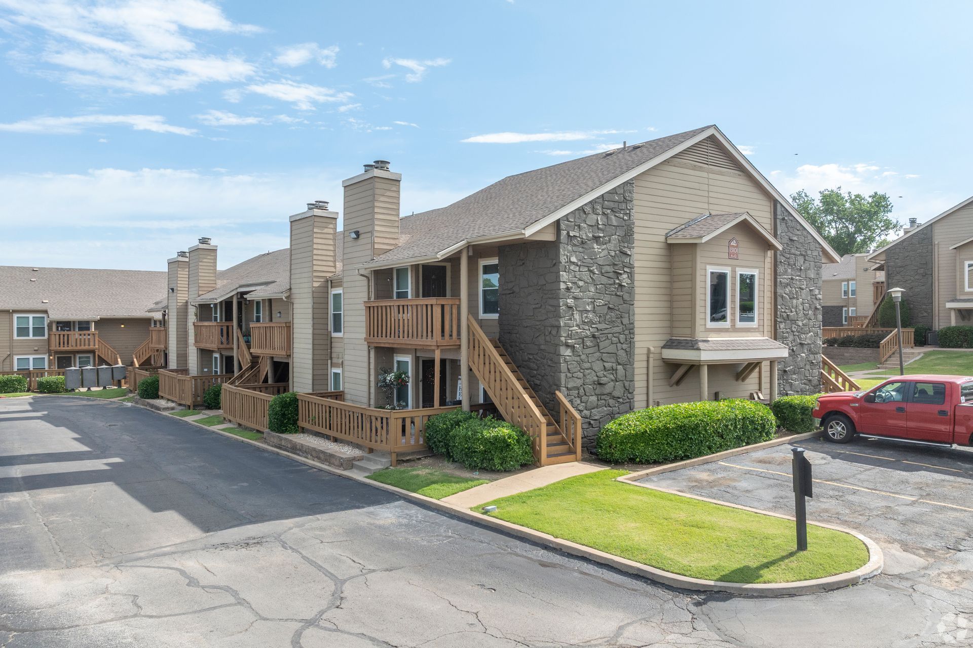 Apartment complex exterior with brick townhomes, staircases, parking lot, and a red car