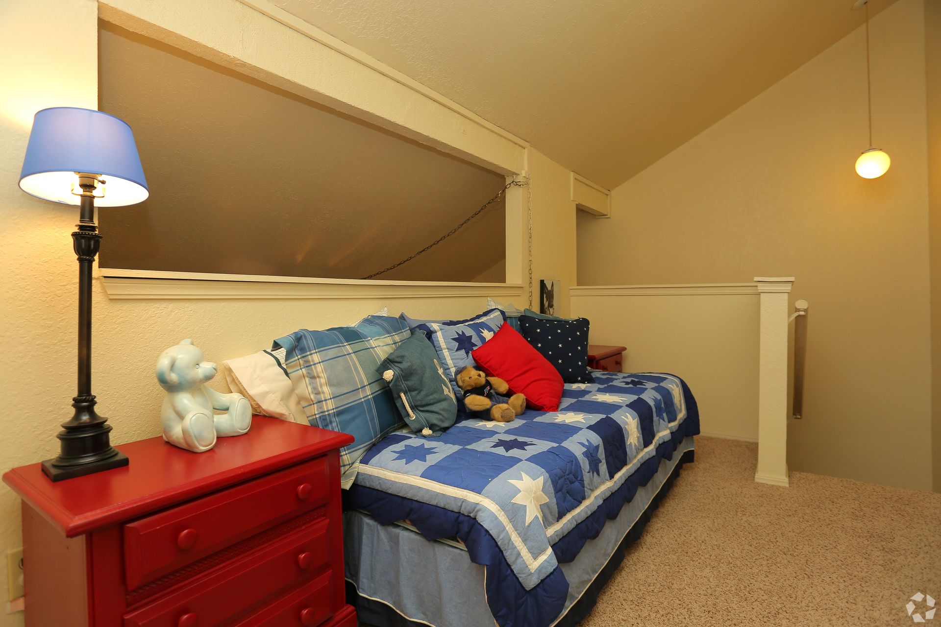 Cozy attic bedroom with blue star quilt, red nightstand, teddy bear, and floor lamp