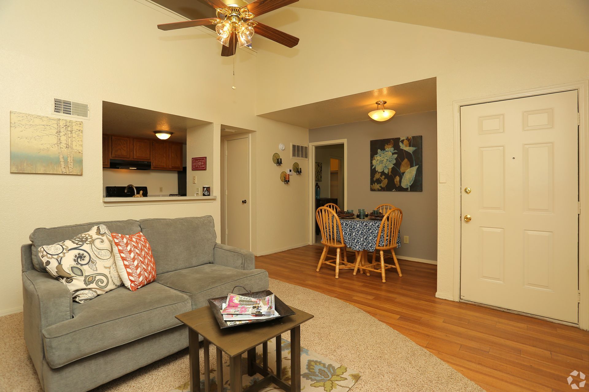 Cozy living room with gray sofa, coffee table, dining nook, hardwood floors, and ceiling fans