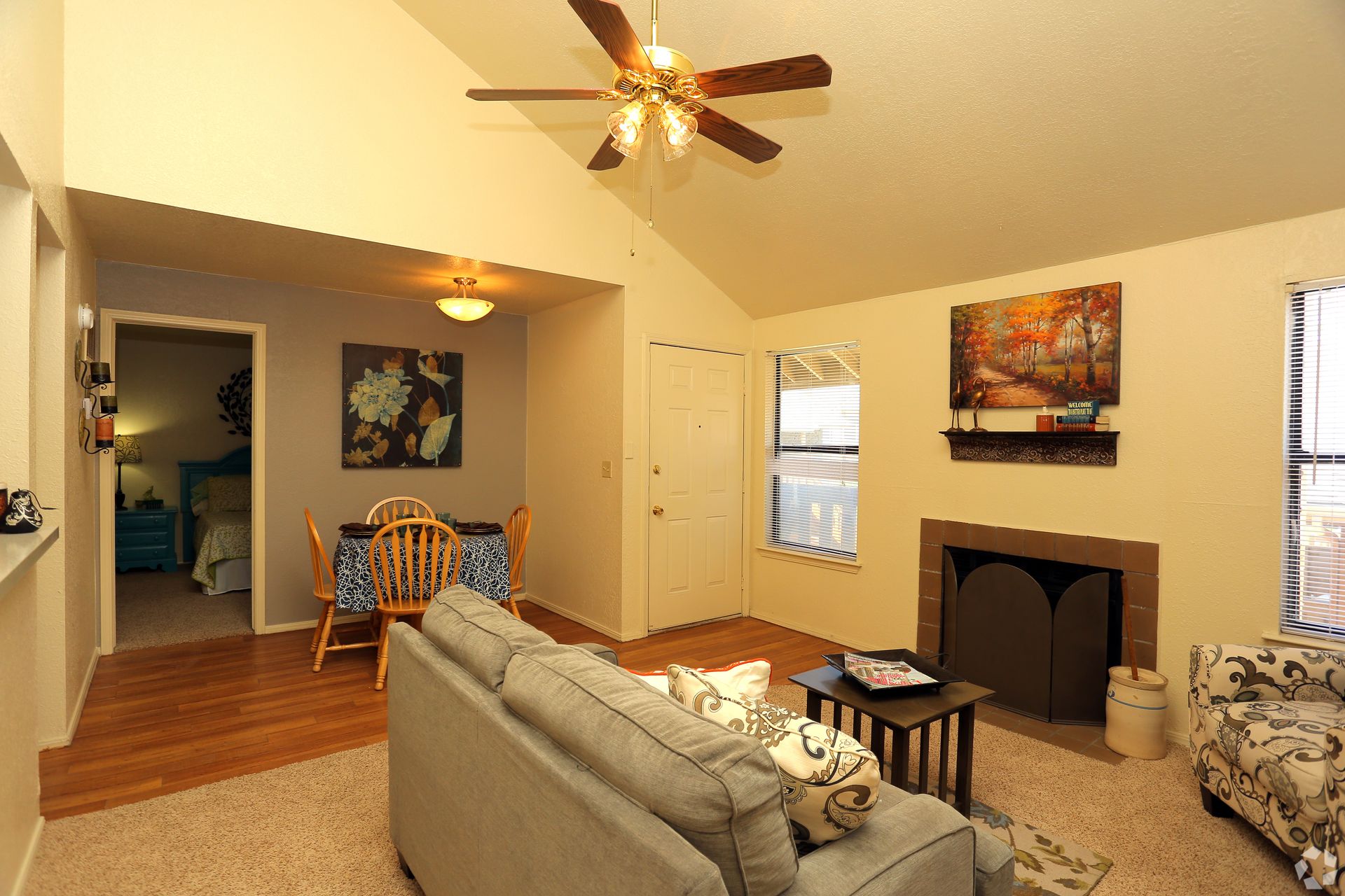 Bright living room with fireplace, ceiling fan, sofa, dining area, and hardwood floors