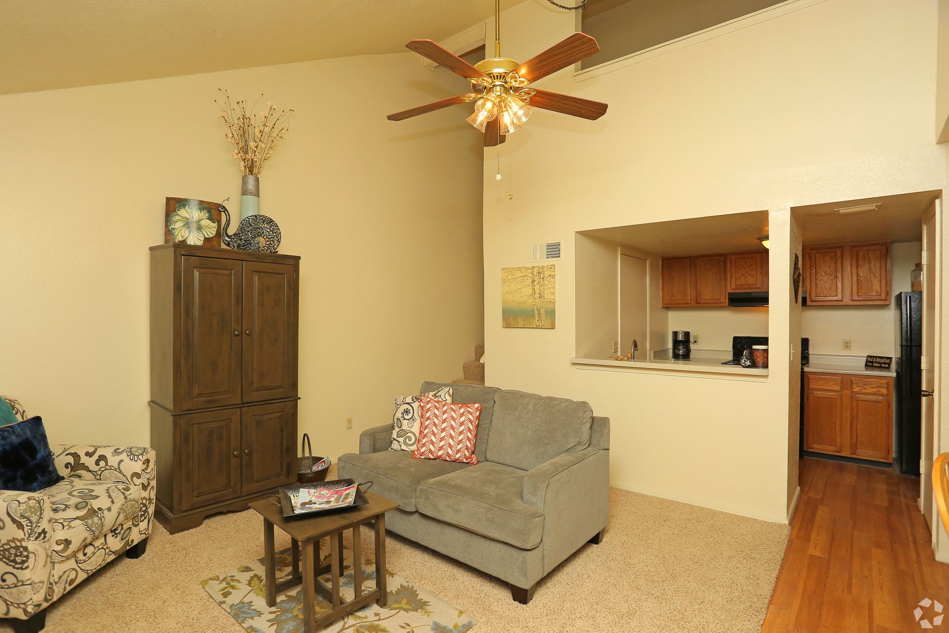 Living room with gray sofa, floral chair, coffee table, tall cabinet, and pass-through to kitchen