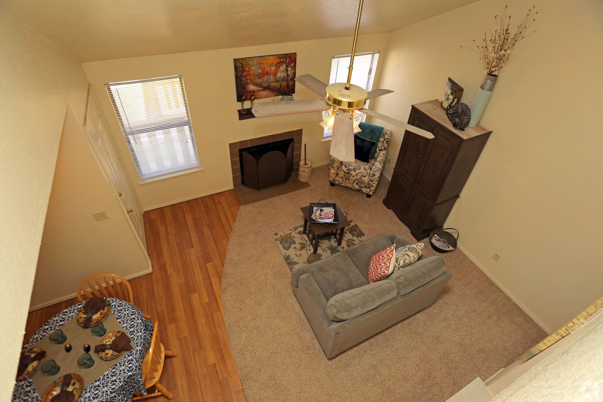 Cozy living room with gray sofa, fireplace, dining table, and hardwood floors, viewed from above.