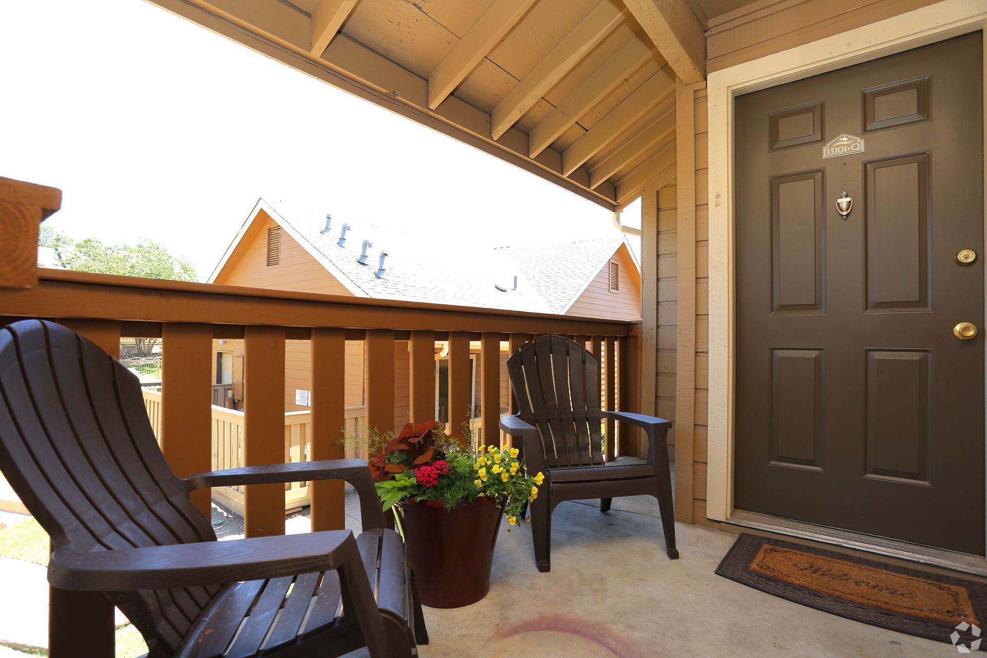 Covered porch with two chairs, a potted plant, and a front door in warm sunlight