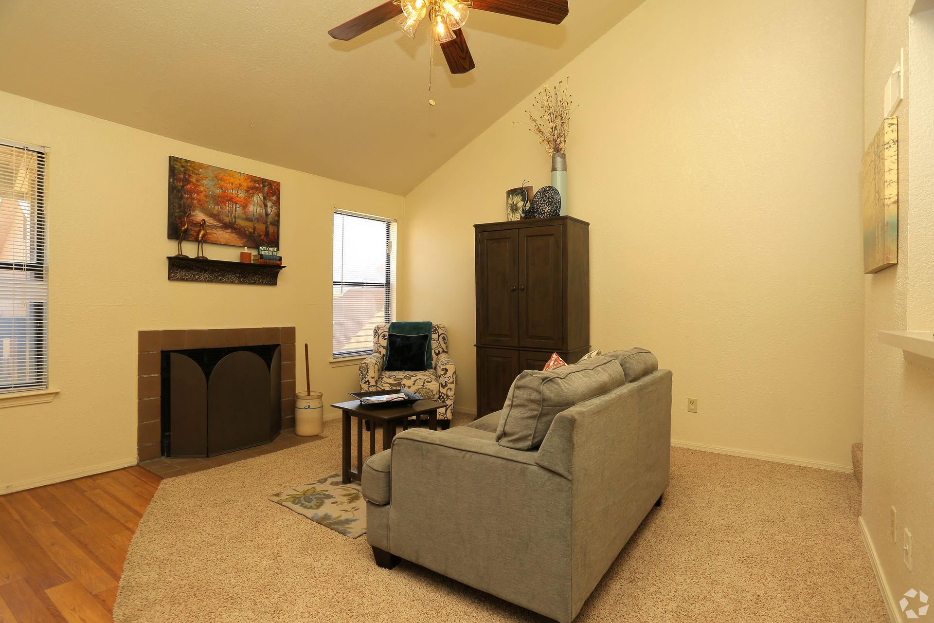 Empty living room with gray sofa, fireplace, carpeted floor, and ceiling fan