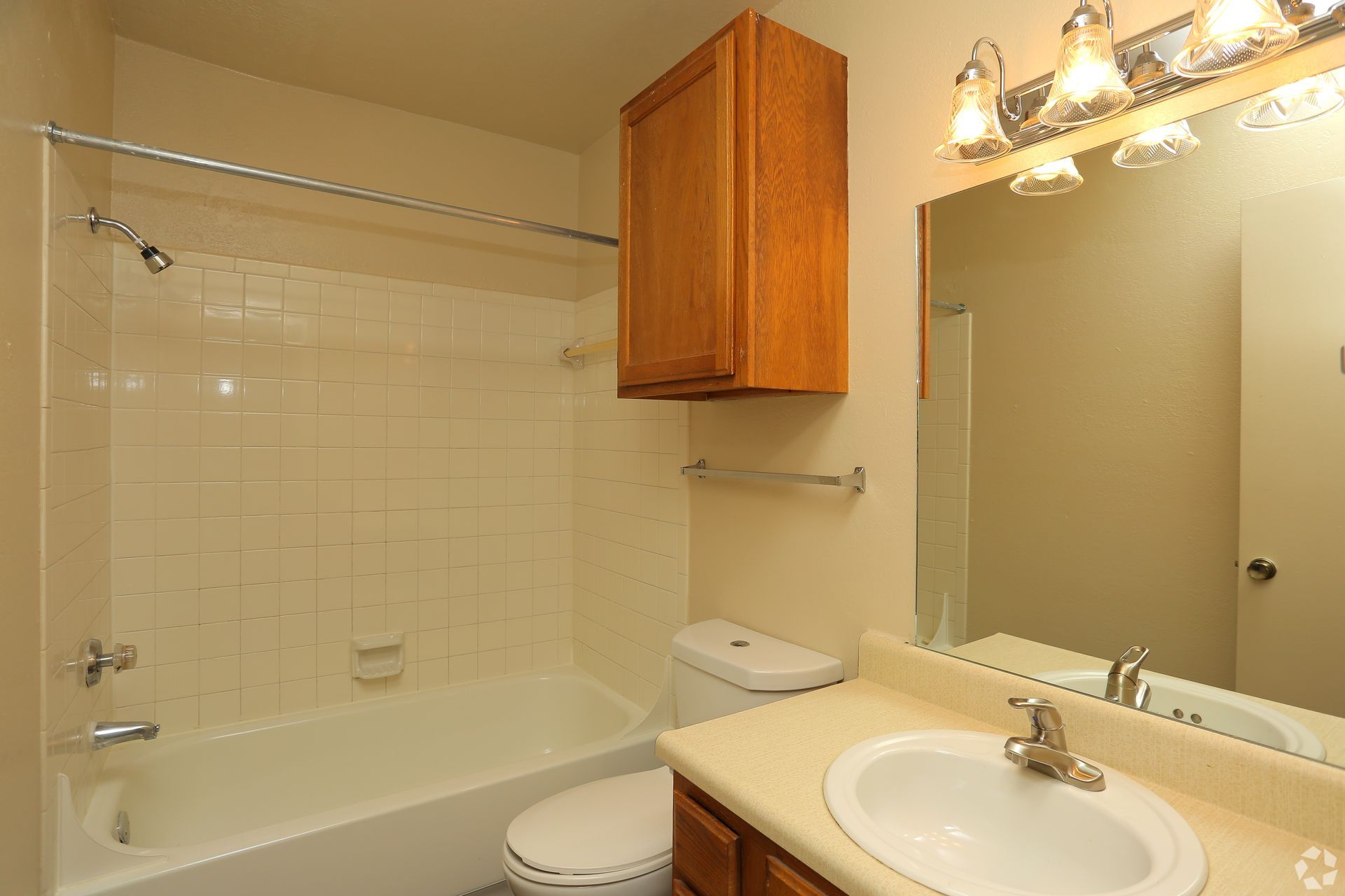 Bathroom with shower-tub, toilet, vanity sink, mirror, and wooden cabinet under warm lighting