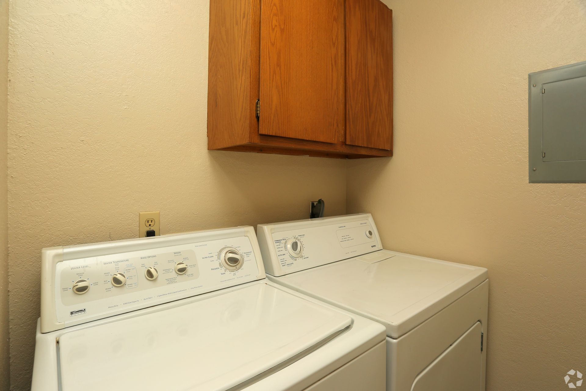 Laundry room with a white washer and dryer beneath a wooden cabinet.