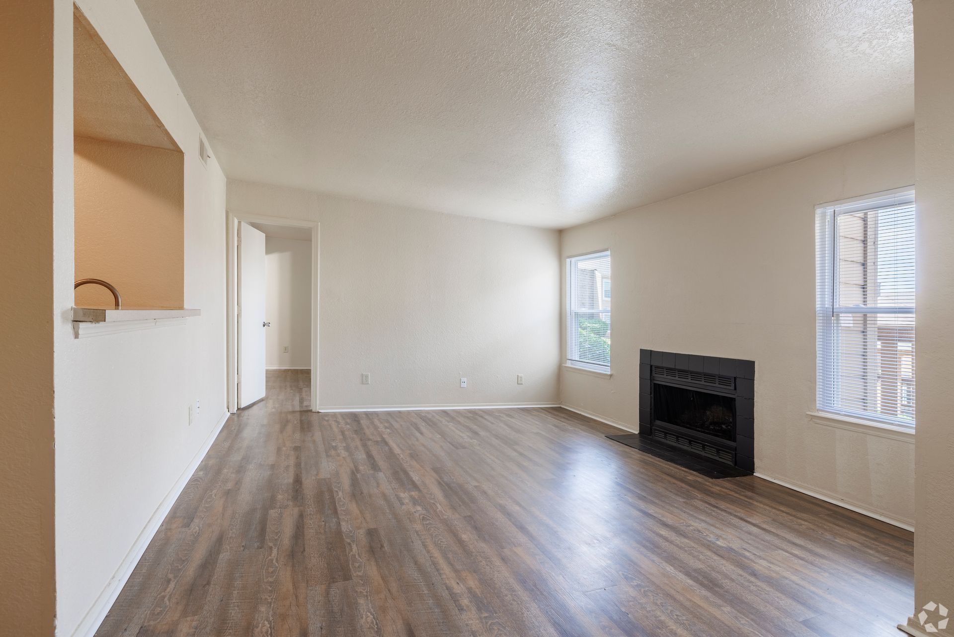 Empty living room with wood floors, white walls, fireplace, and windows letting in light