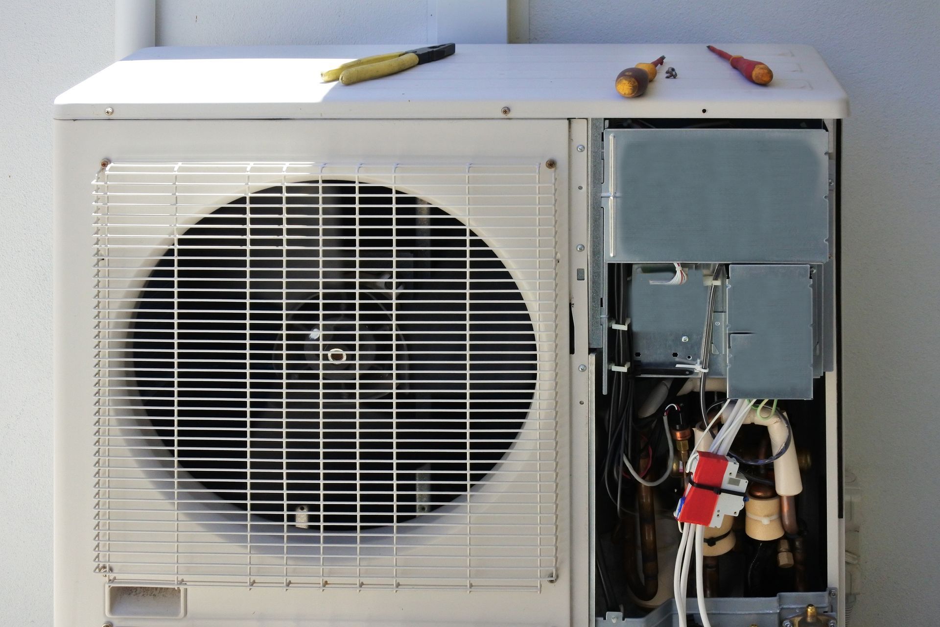 An air conditioner is being repaired with tools on top of it.
