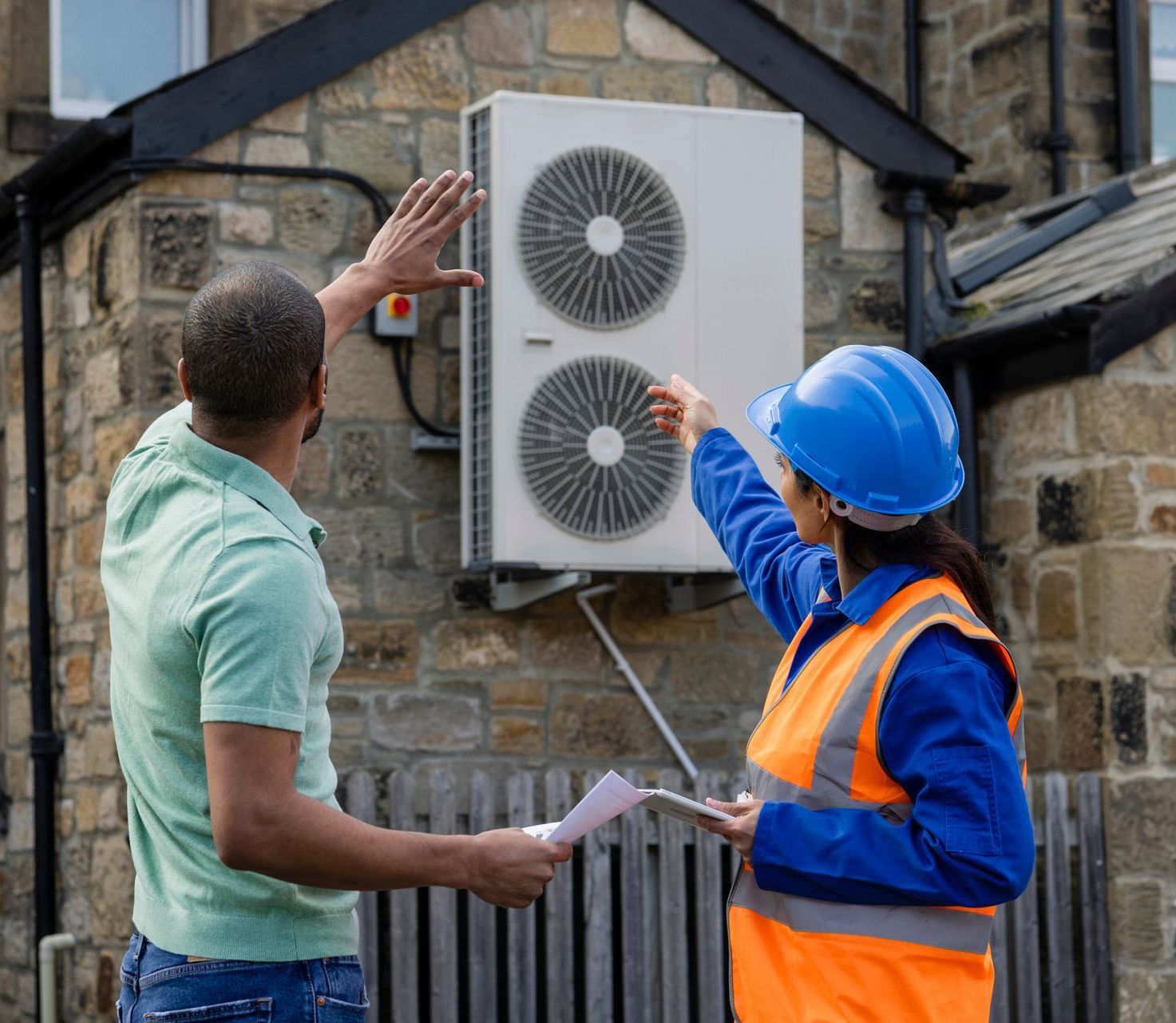 A man and a woman are looking at an air conditioner on the side of a building.