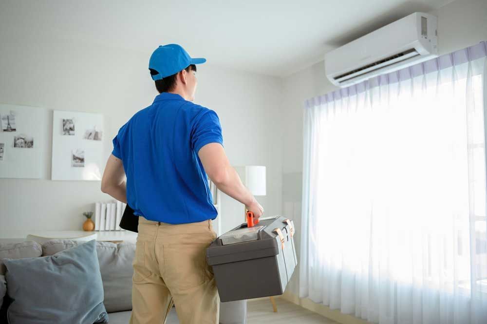 An air conditioning repair contractor, holding tools and in a blue uniform, is about to check an AC.