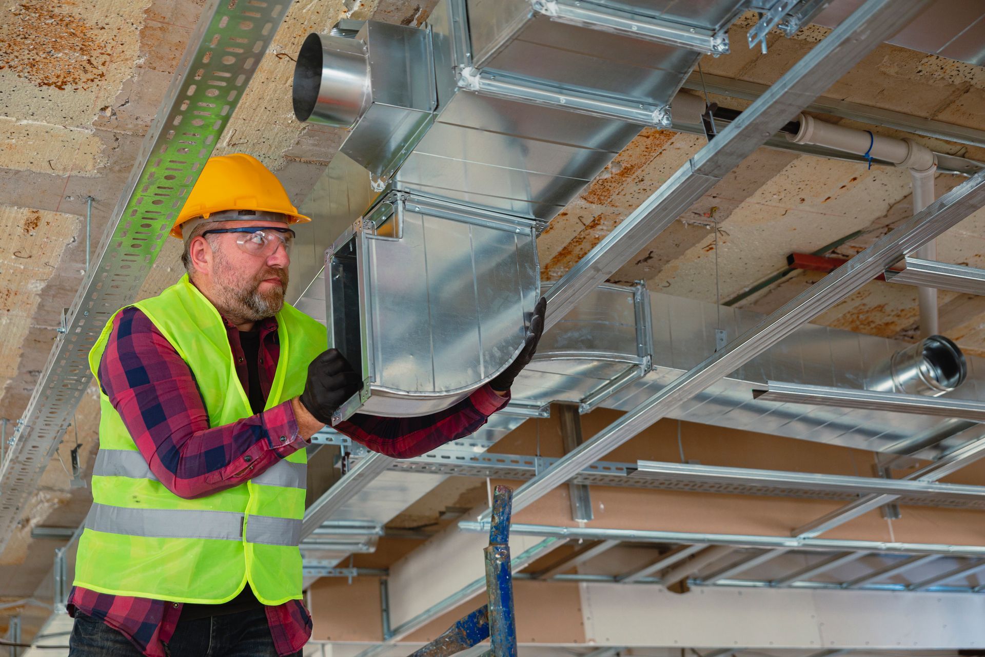 A man is working on a ventilation system in a building under construction.