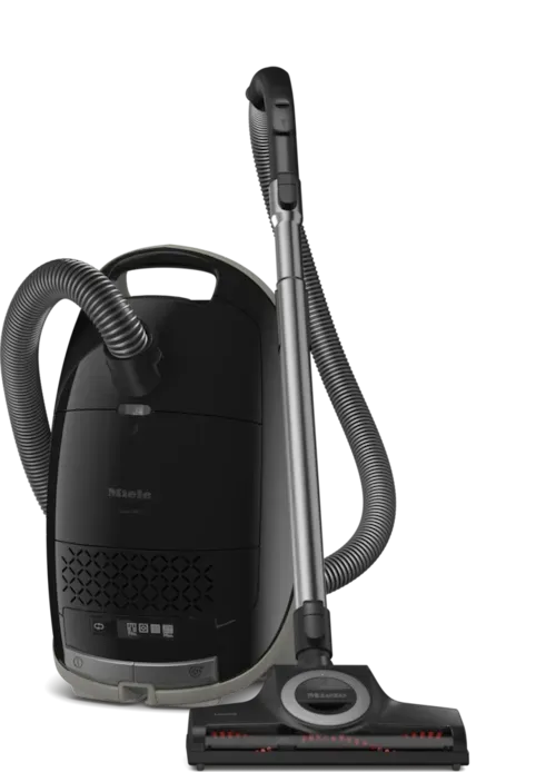 Black Miele canister vacuum cleaner with attachments, standing on a white background.