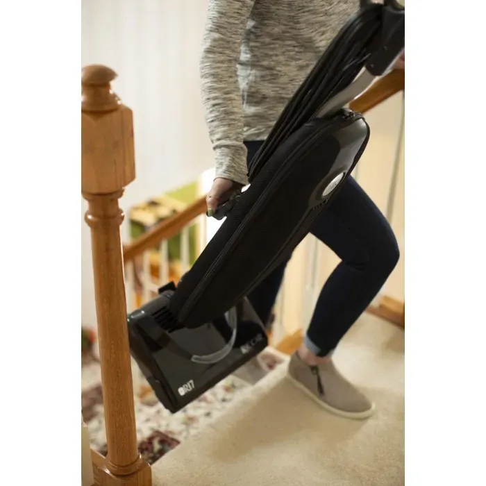 Person carrying a black vacuum cleaner up carpeted stairs.