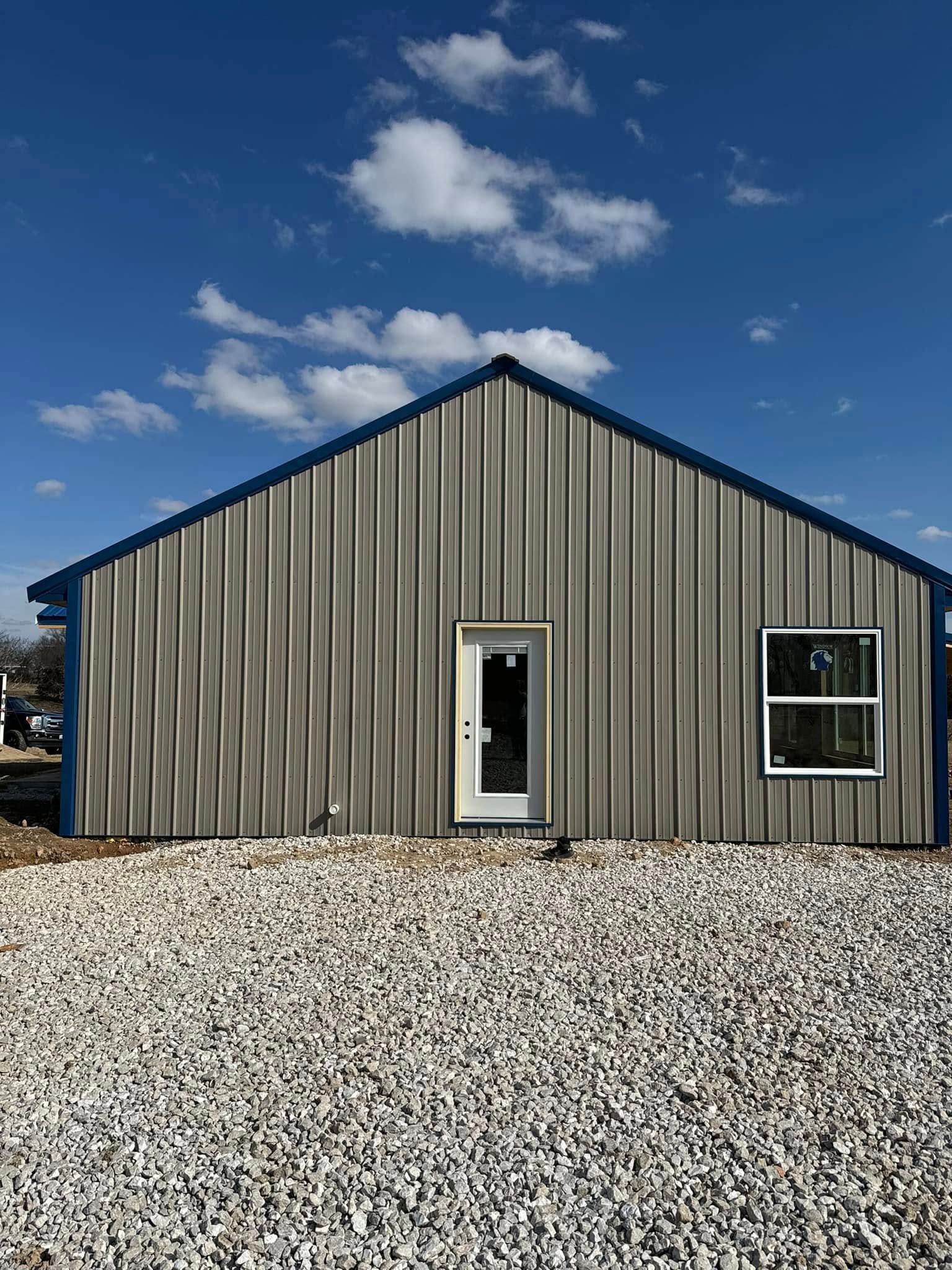 Gray metal-sided building with a door and window, set against a blue sky with clouds.
