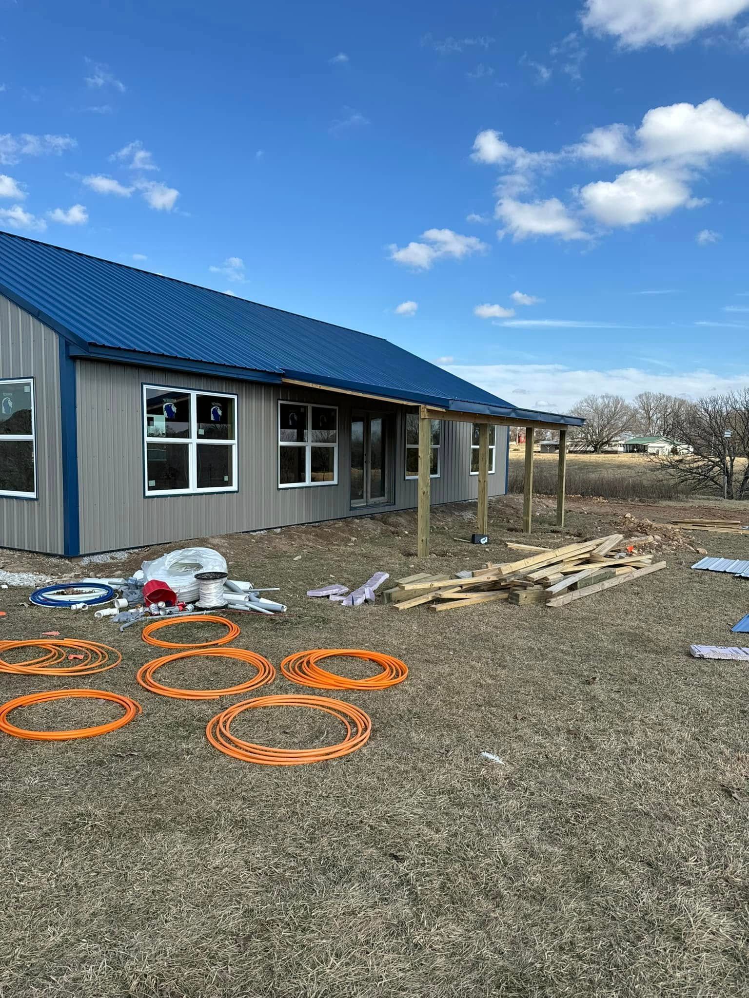 Exterior view of a building under construction with a blue roof, windows, and materials scattered on the ground.