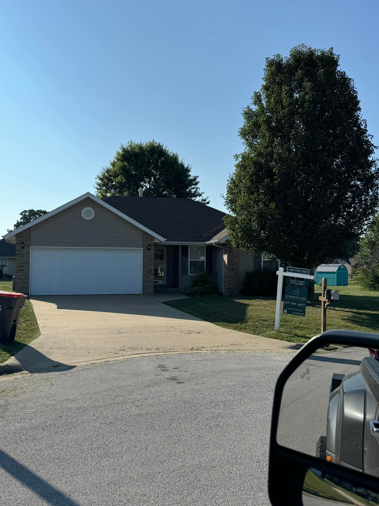 A single-story house with a driveway. A tree stands beside the house. Blue sky overhead.