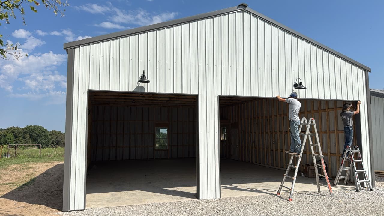 Two workers installing lights on a white metal garage with two bays.