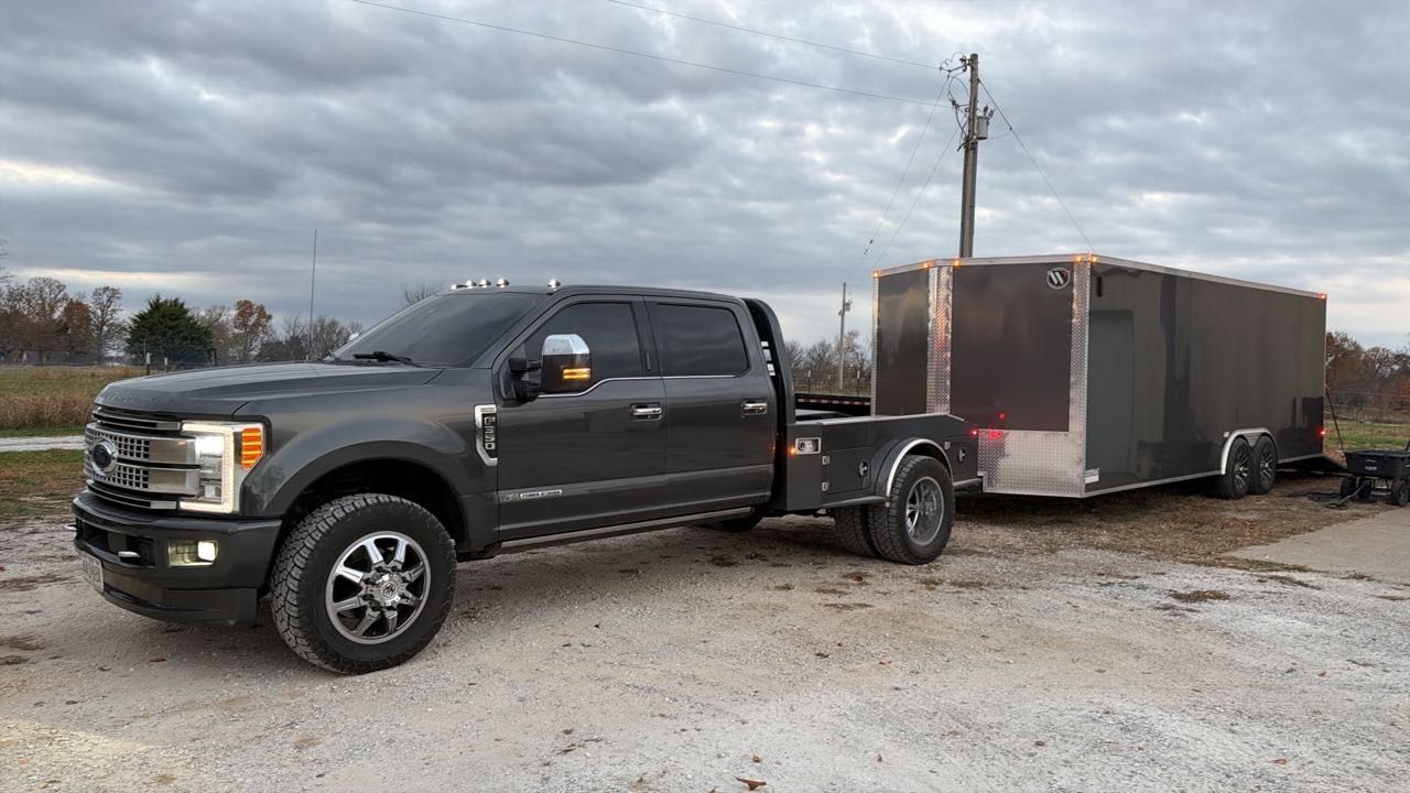 Dark gray pickup truck with a trailer parked on gravel under a cloudy sky.