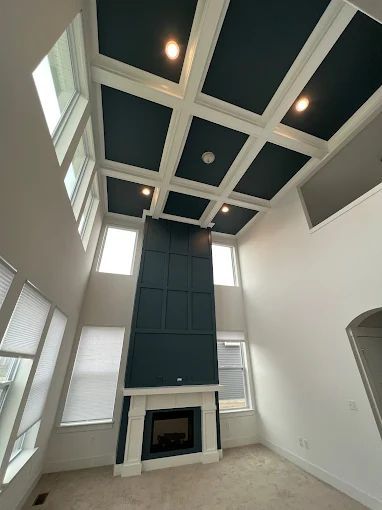 High-ceilinged room with a teal fireplace, coffered ceiling, and tall windows.