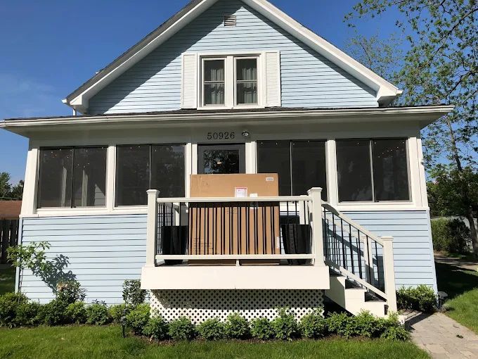 A light blue house with a porch. A large cardboard box sits on the porch.