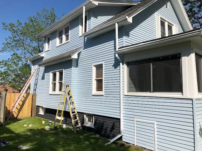 Light blue house with white trim, ladders, and a wooden fence.
