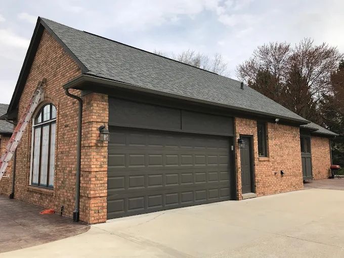 Brick garage with dark brown garage door, roof, and trim. Cloudy sky.