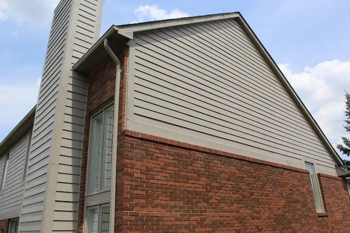 Brick and beige-sided house exterior with a chimney, windows, and a blue sky.