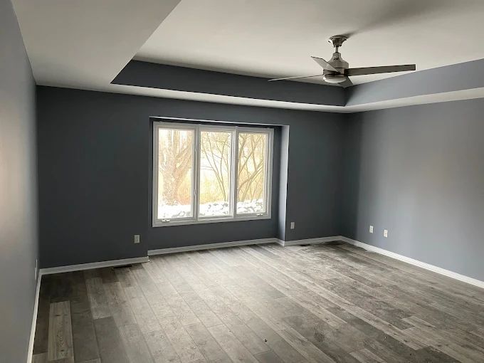 Empty room with gray walls and flooring, three-panel window, ceiling fan, and recessed ceiling.