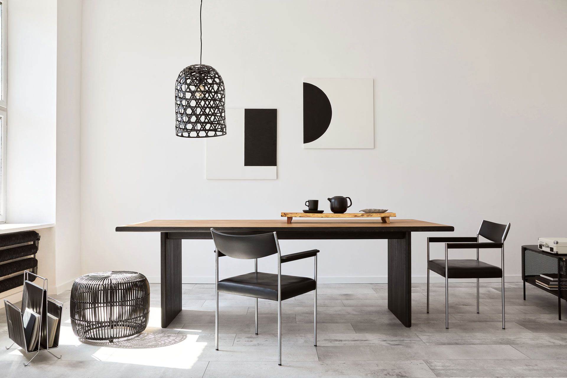Modern dining room with a long table, black chairs, and abstract art on white walls.