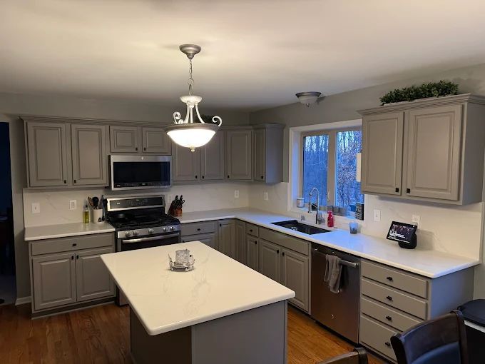 Gray kitchen with white countertops and island, stainless steel appliances, and wood flooring.