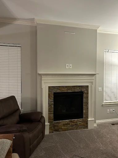 Fireplace with stone accent, white mantel, grey wall, recliner in foreground.