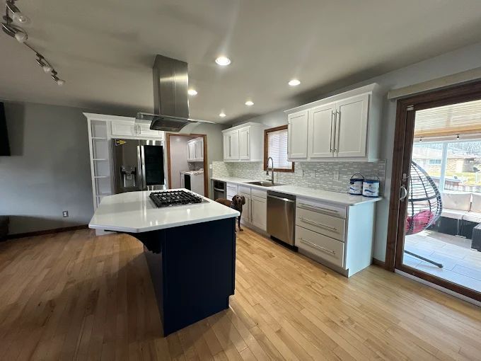Modern kitchen with white cabinets, blue island, stainless steel appliances, and hardwood floors.