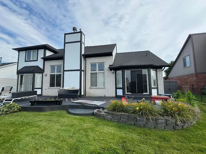 Back exterior of a two-story brick house with black trim. A chimney, patio and lawn are visible.