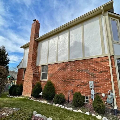 Brick house with a chimney and white siding under a blue sky.