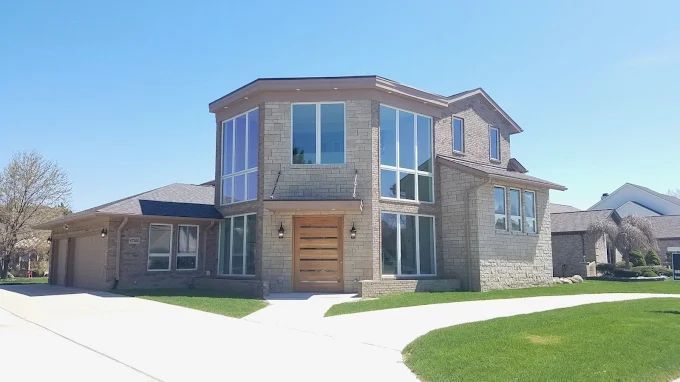 Two-story brick house with large windows under a blue sky, driveway, and green lawn.