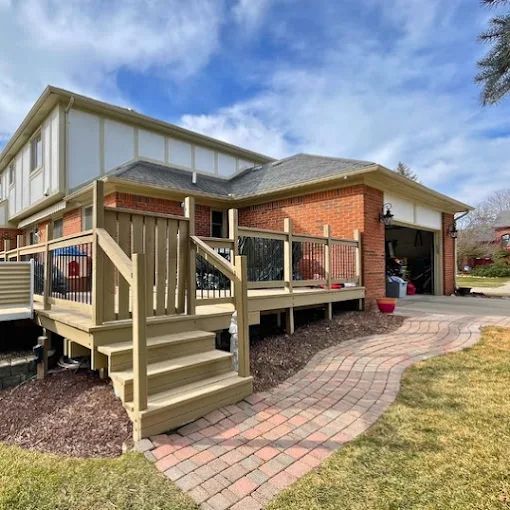 Wooden deck with stairs attached to a brick house, a brick walkway, and a garage.