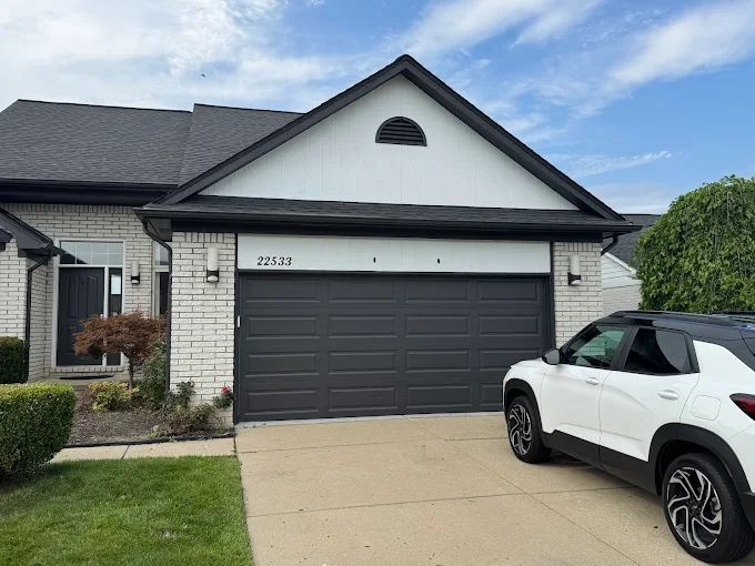 House with dark gray garage door, white brick, black trim, and a white SUV in the driveway.